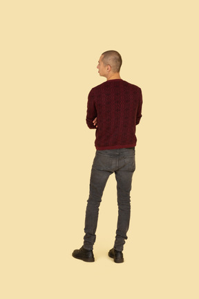 Back view of a pouting young man dressed in casual clothes crossing his hands