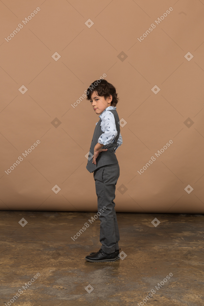 Vista laterale di un ragazzo in abito grigio in piedi con le mani sui fianchi