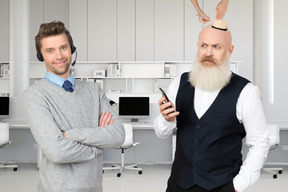 Man with headset standing next to bearded man with tiny hat