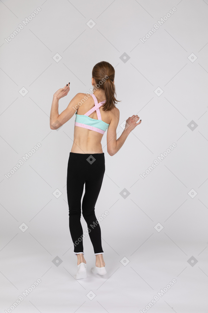 Three-quarter back view of a teen girl in sportswear raising hands while balancing