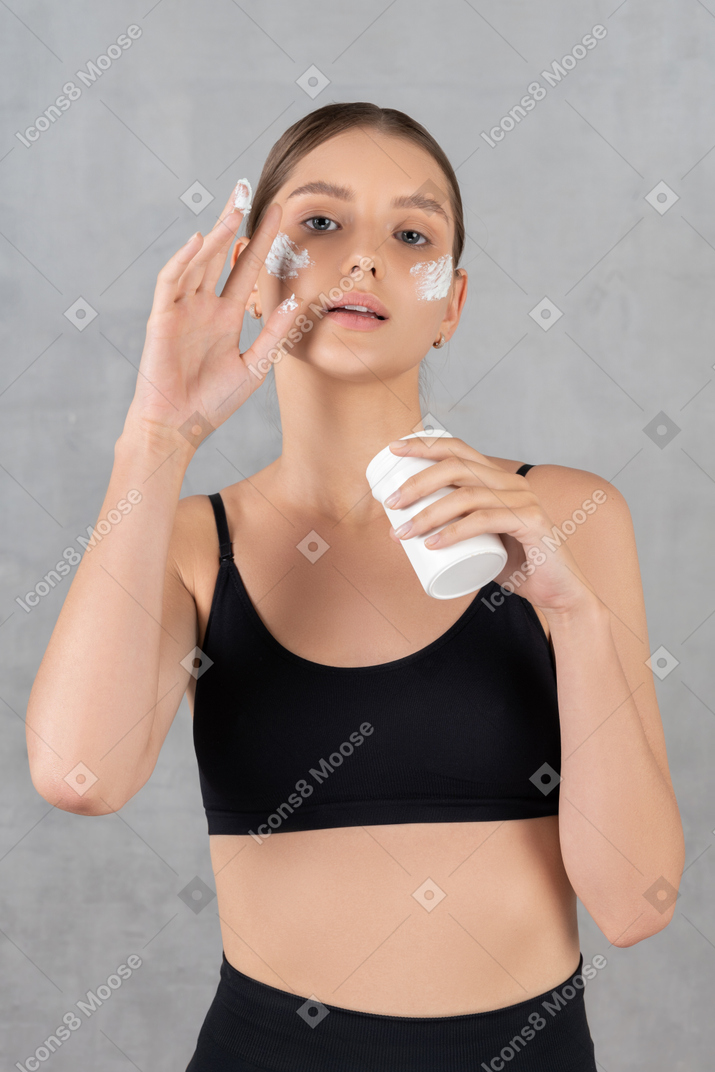 Mujer hermosa joven que aplica crema facial en su piel