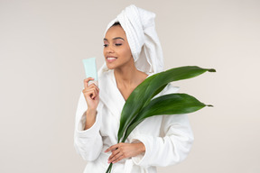 Mulher negra no roupão branco e toalha de cabeça, desfrutando de sua rotina de cuidados da pele