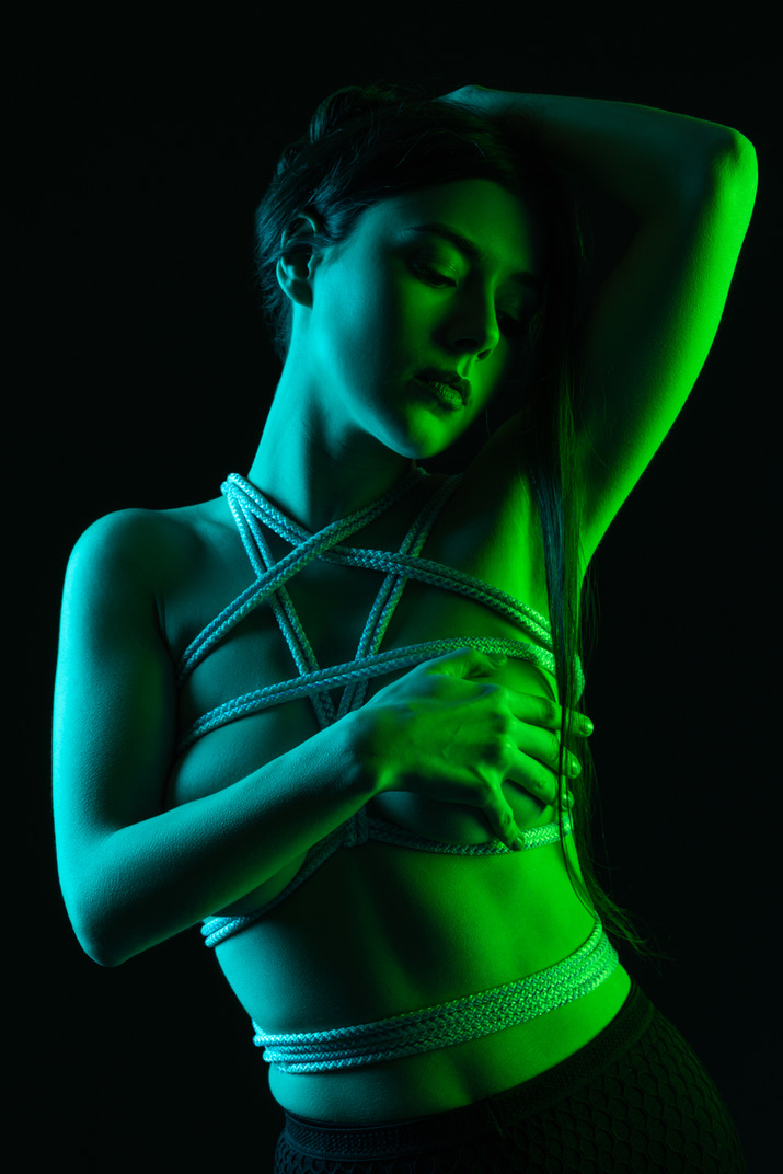 A sensual shot of a woman in harness posing under green light