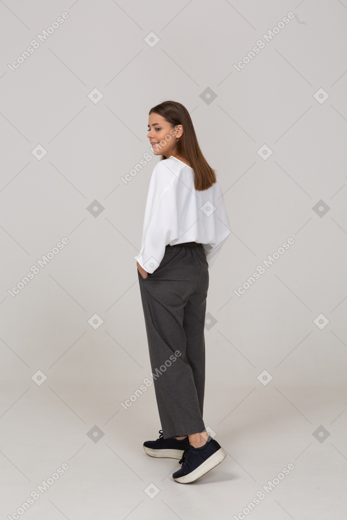 Vue de trois quarts arrière d'une jeune femme en vêtements de bureau se mordant les lèvres en marchant