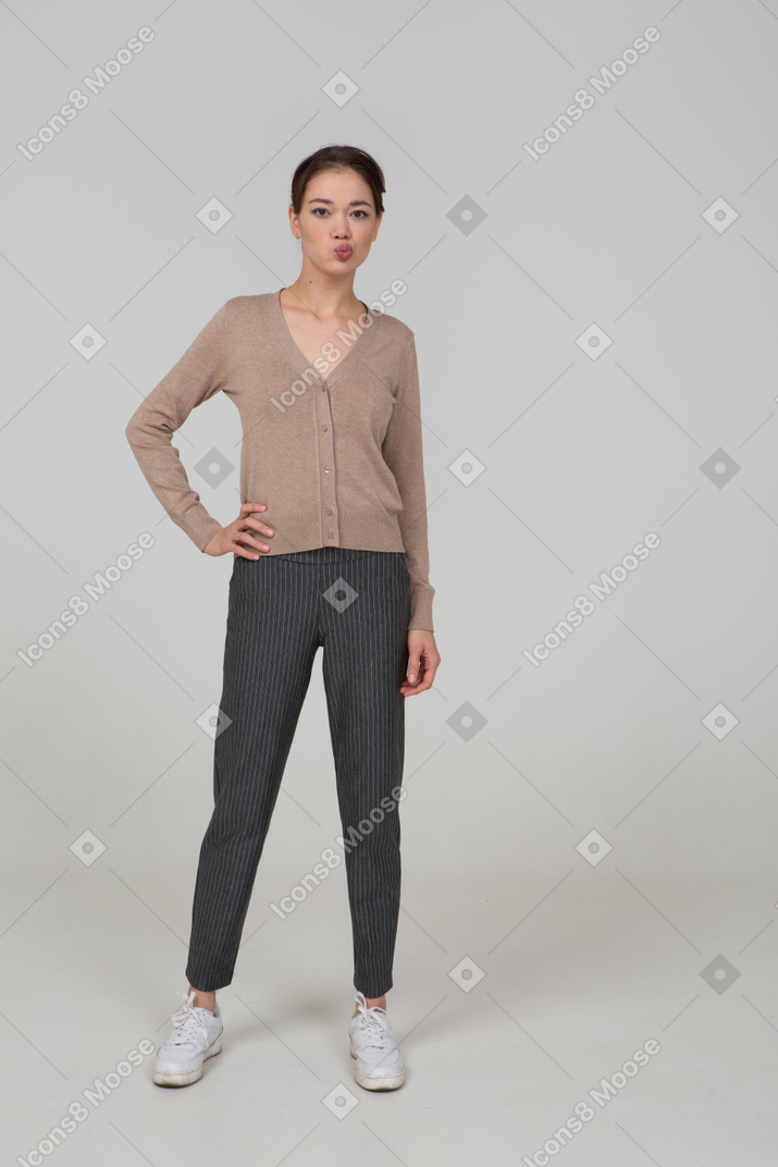 一位年轻的女士，仍然站在套头衫和裤子，把手放在臀部上，uting着嘴的前视图