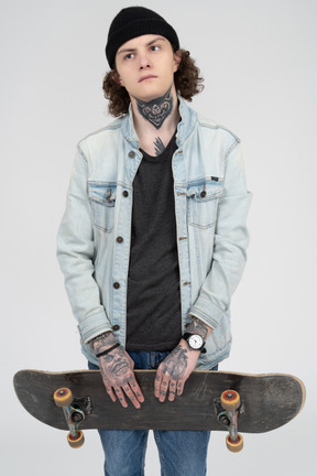 Adolescente tatuato che tiene uno skateboard