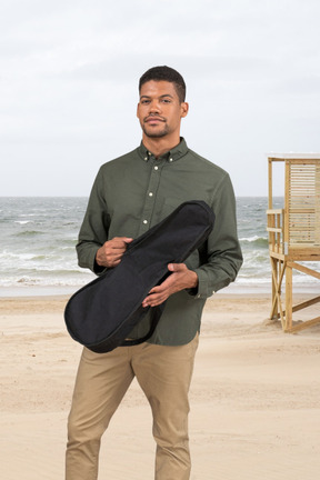 Hombre con estuche de guitarra en la playa
