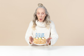 歳の女性が彼女の百と五歳の誕生日のケーキの上のろうそくを吹き