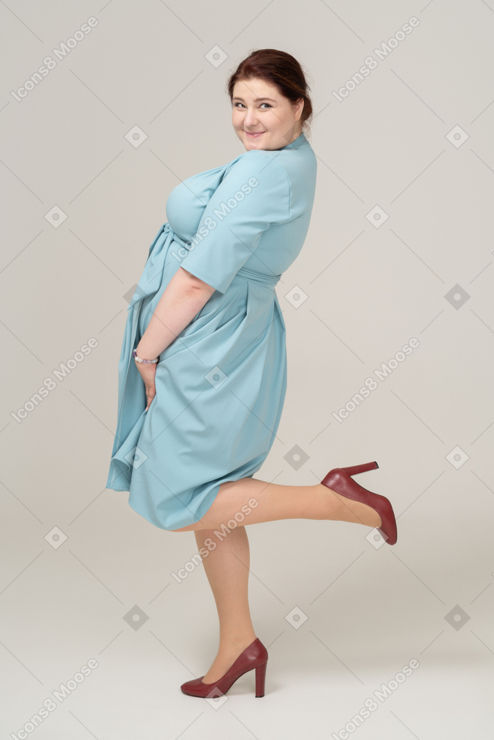 一个穿着蓝色连衣裙、单腿摆姿势的女人的侧视图