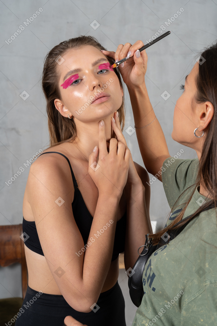 Porträt einer attraktiven frau, die posiert und eine make-up-künstlerin, die lidschatten aufträgt