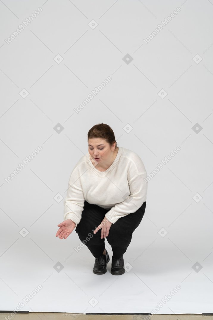 Front view of a plus size woman in white sweater squatting