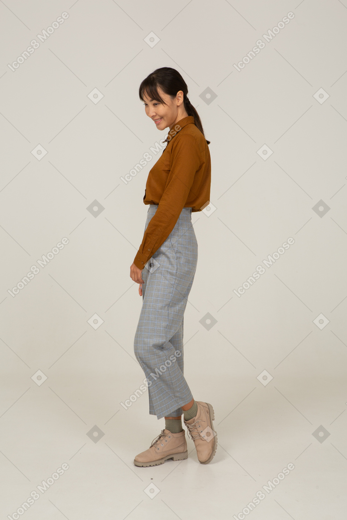 Vista laterale di una giovane donna asiatica sorridente in calzoni e camicetta