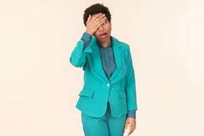 Black woman with a short haircut, wearing all blue, standing against a plain pastel background, looking emotional