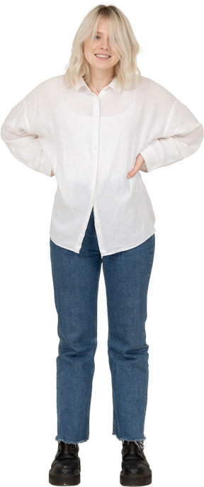Vista frontale di una donna bionda in abiti casual, mettendo le mani sui fianchi e sorridente