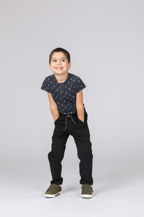 Front view of a happy boy in casual clothes posing with hands in pockets and looking at camera