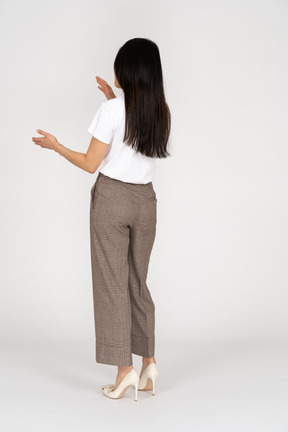 Vista posterior de tres cuartos de una mujer joven con pantalones y camiseta blanca que muestra el tamaño de algo