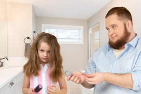 A man combing a little girl's hair in a bathroom