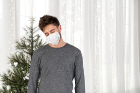 A man wearing a face mask in front of a christmas tree