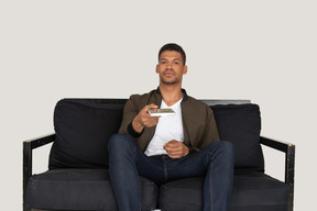 Front view of young man sitting on a sofa and passing pensil with notebook