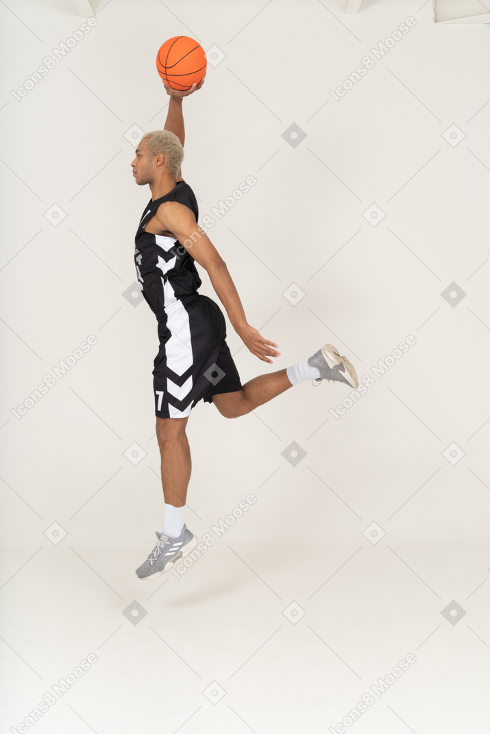 Vista laterale di un giovane giocatore di basket maschile che segna un punto