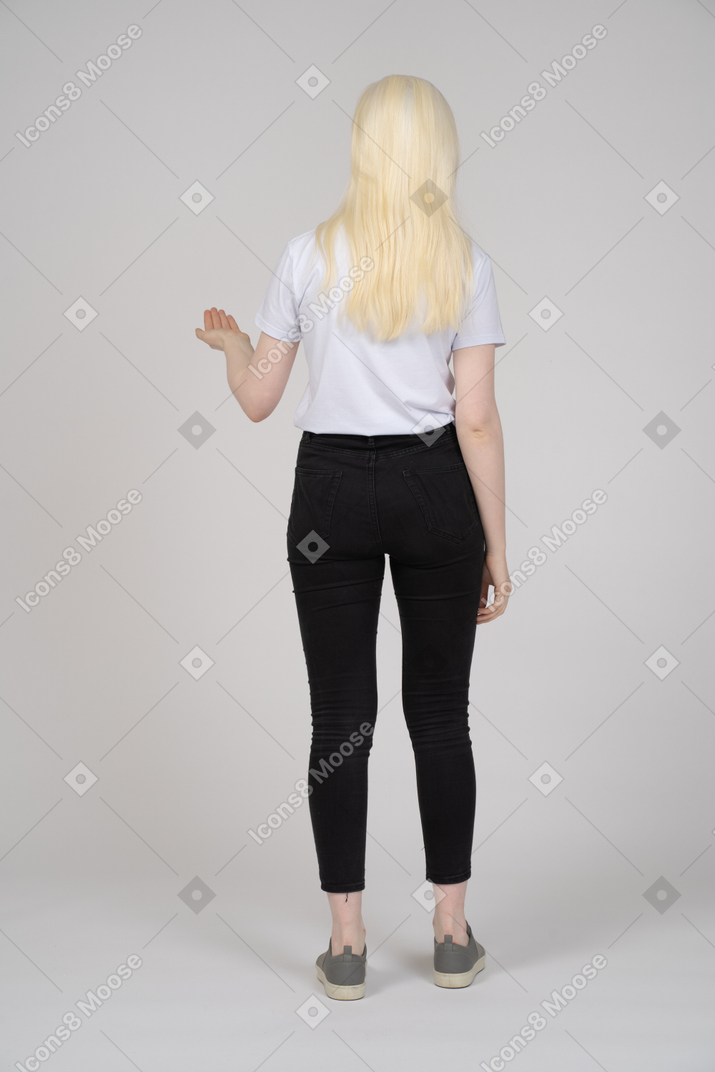 Back view of a young blonde girl standing and holding up hand