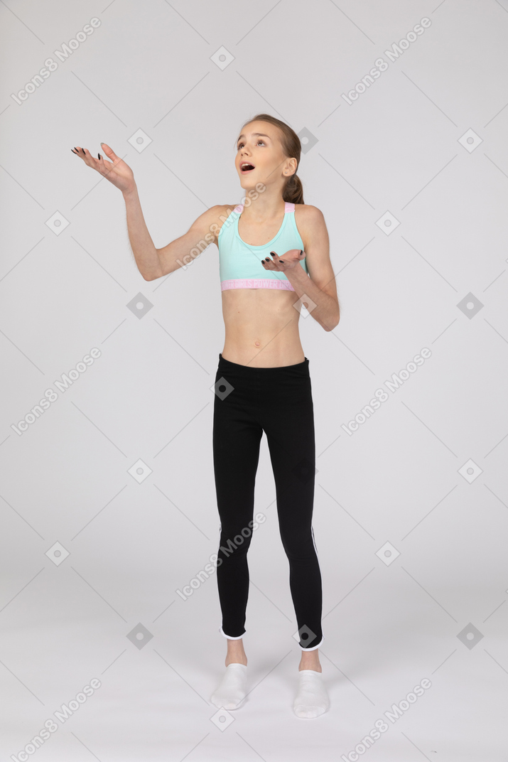Vista frontal de uma adolescente surpresa em roupas esportivas, levantando as mãos e abrindo a boca