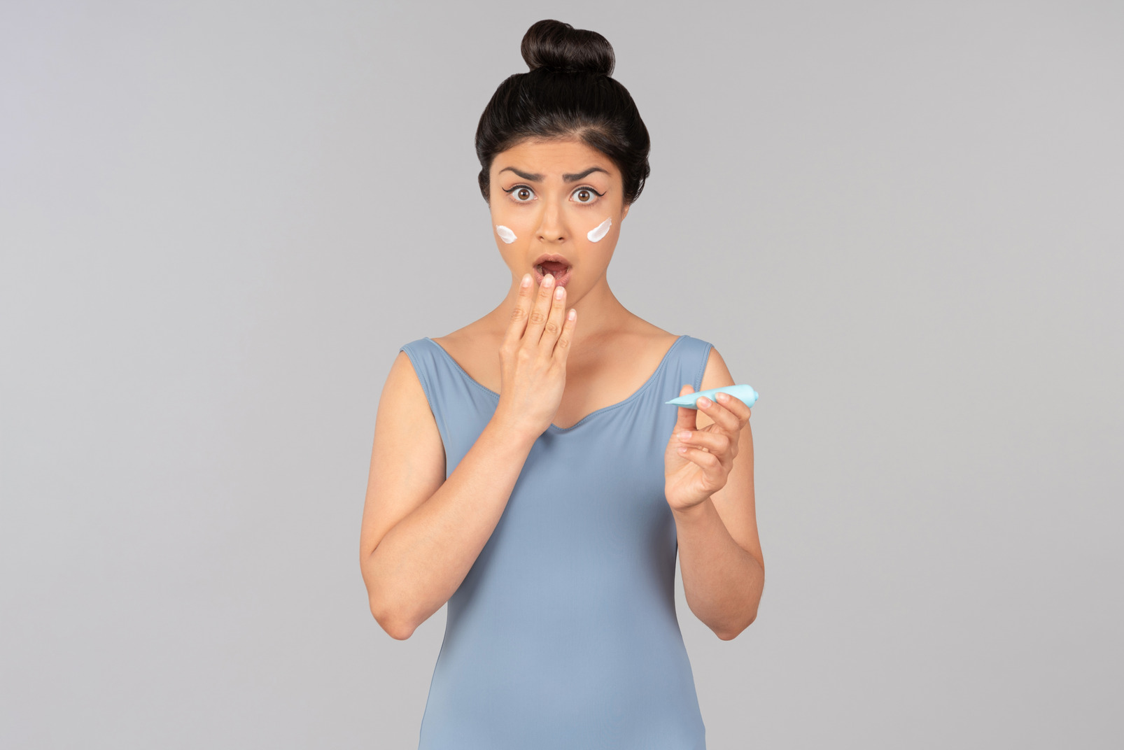Gasping young indian woman holding face cream