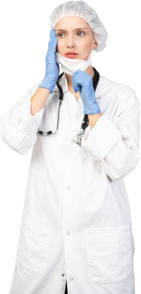 Vista frontal de uma jovem médica colocando uma máscara e olhando para o lado