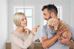 A man and woman feeding a dog in a kitchen