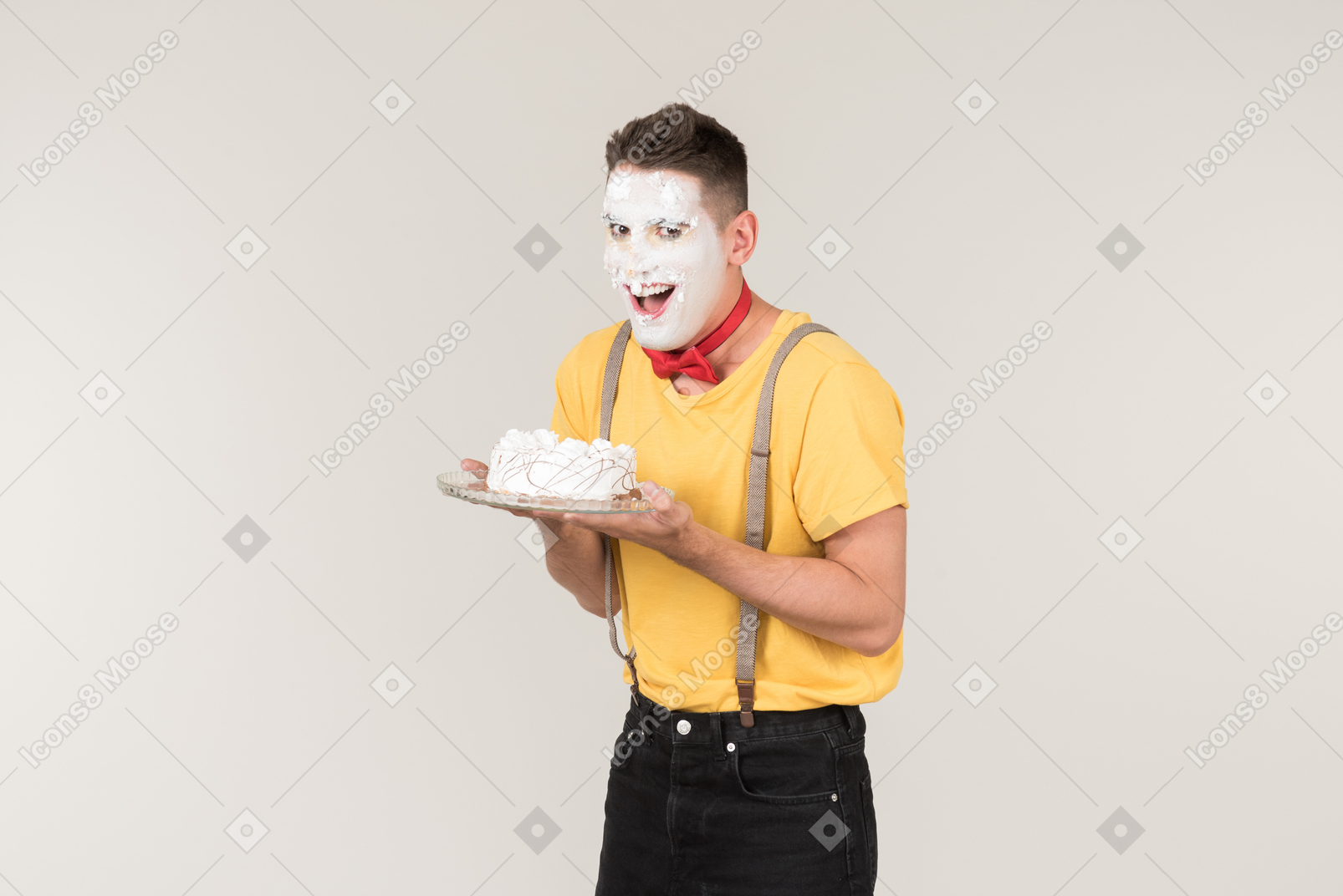 Male clown with cake cream on his face holding a cake