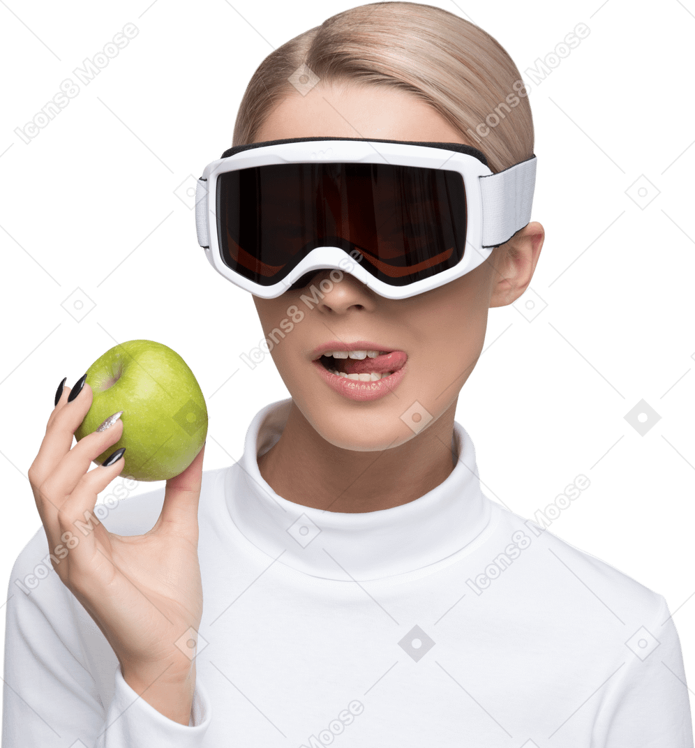 Mujer joven con gafas de esquí sosteniendo una manzana.