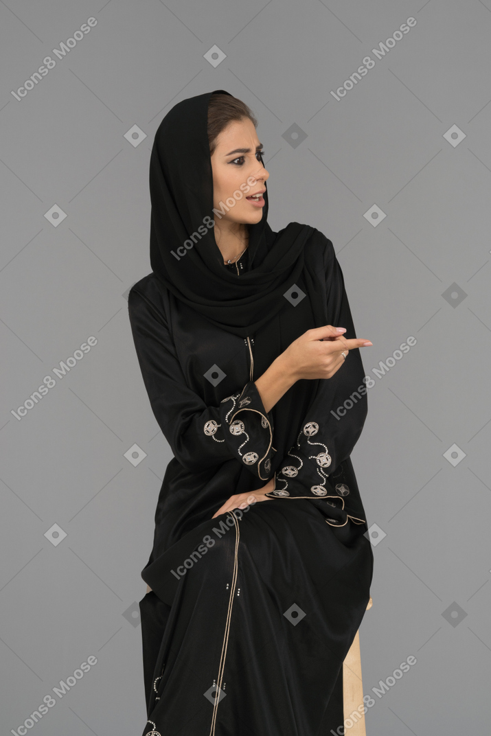 Una mujer árabe escéptica apuntando hacia un lado con un dedo