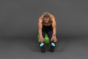 Front view of a shirtless afro man stretching while sitting on a green gym ball