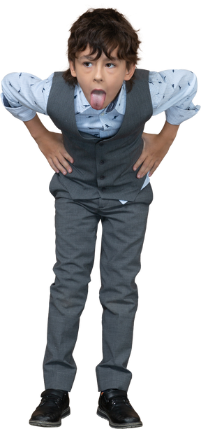 Vista frontal de un niño con traje gris posando con las manos en las caderas y mostrando la lengua