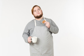A fat man holding a cookie and a cup of coffee