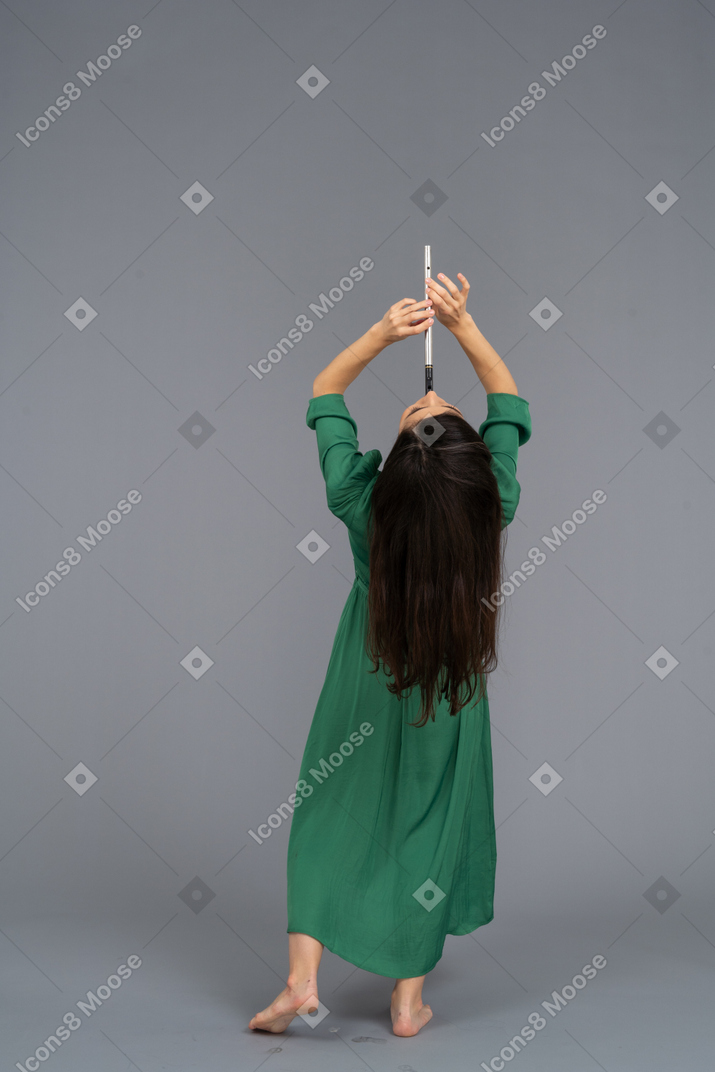 Rückansicht einer jungen dame im grünen kleid, die flöte spielt, während sie sich zurücklehnt