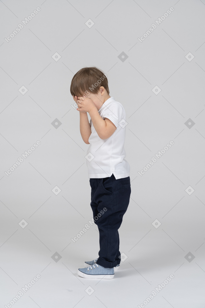 Side view of little boy covering his face with his hands