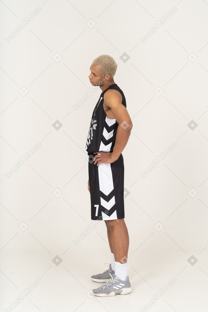 Vista lateral de um jovem jogador de basquete masculino em exercício colocando as mãos nos quadris