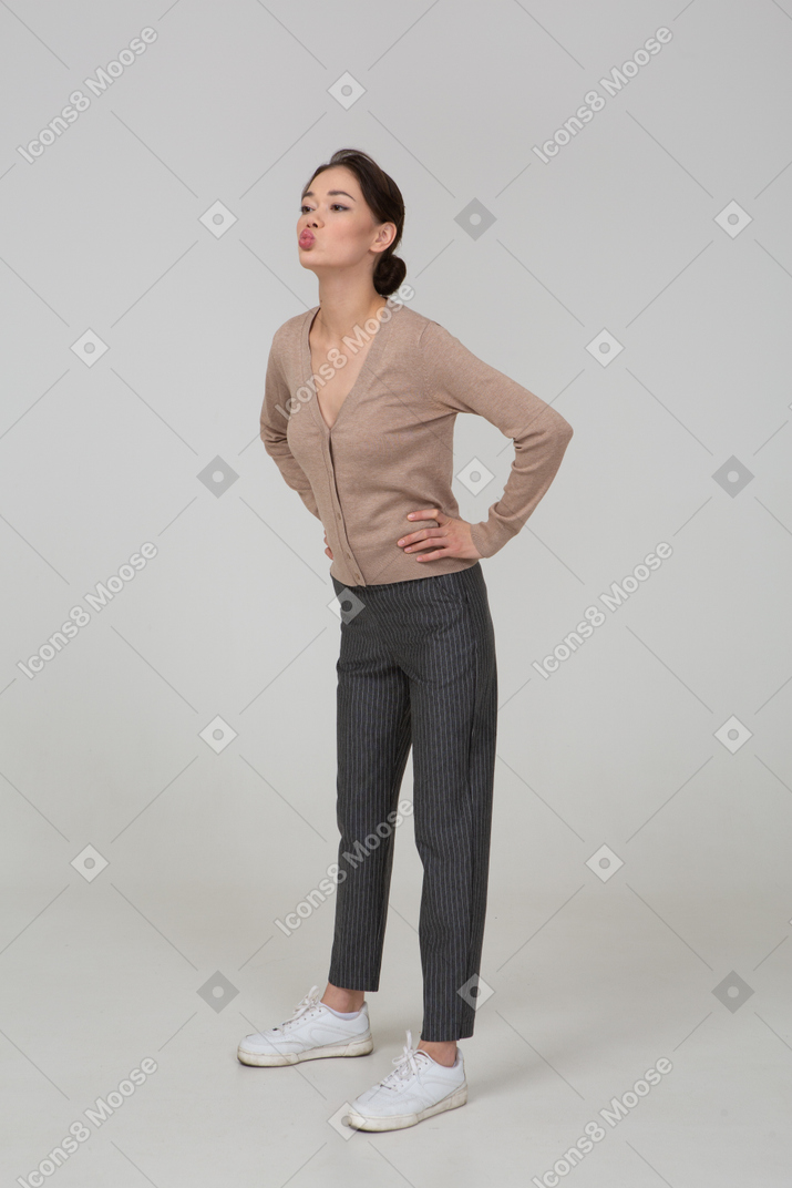 Three-quarter view of a young lady in pullover and pants sending an air kiss and putting hands on hips