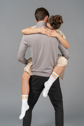 Back view of a young man holding his girlfriend up above the floor