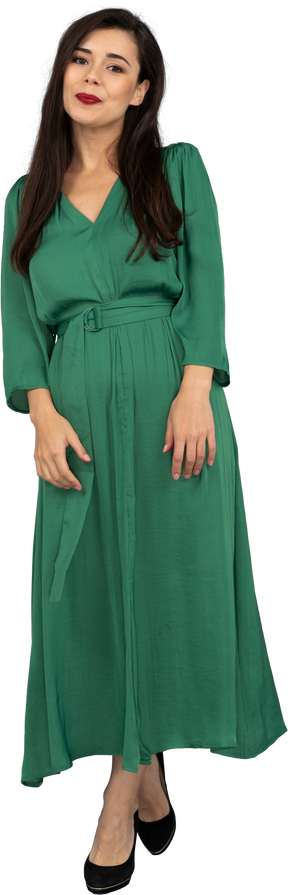 Vista frontal de uma jovem sorridente e tímida em um vestido verde