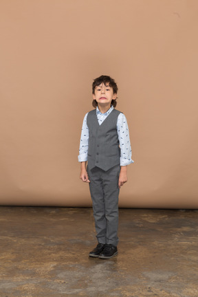 Vista frontal de un niño con traje gris mirando a la cámara y haciendo muecas