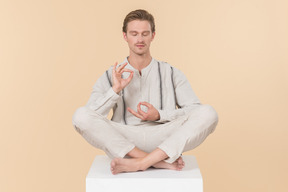 Young man sitting in lotus pose and showing ok sign