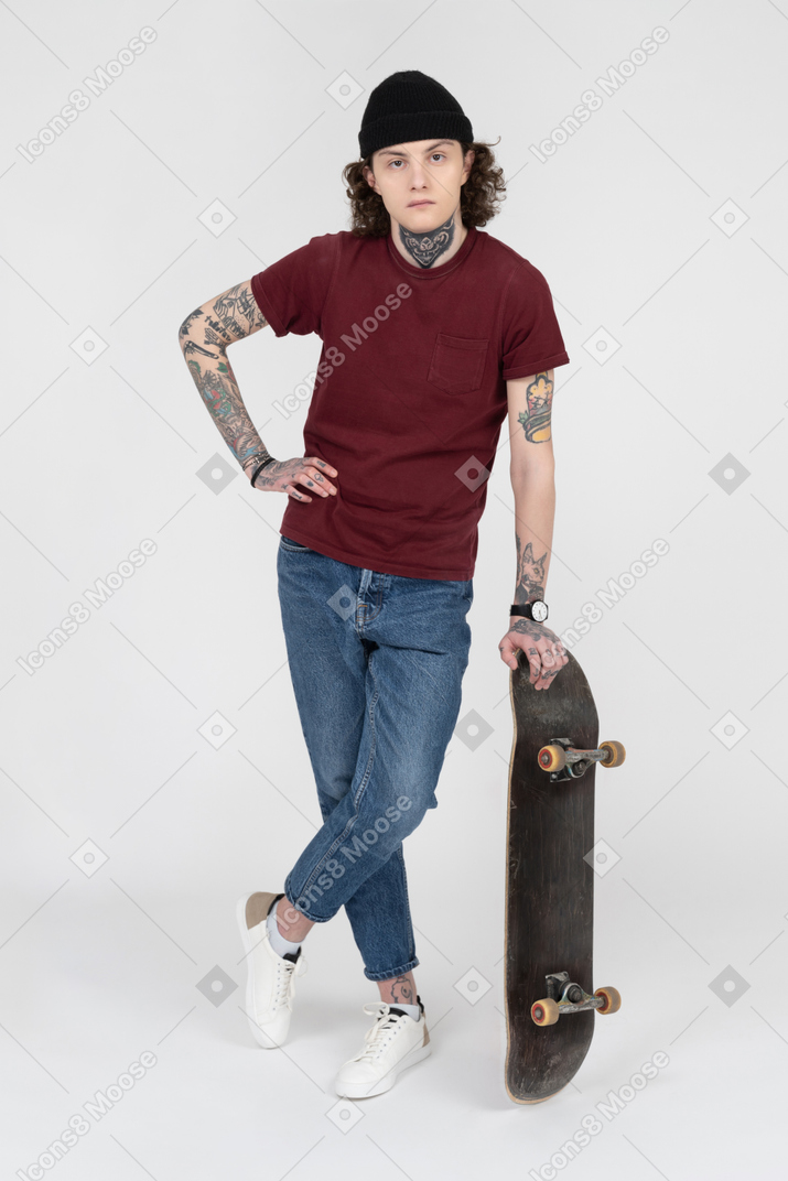 彼のスケートボードを持って立っているティーンエイジャー