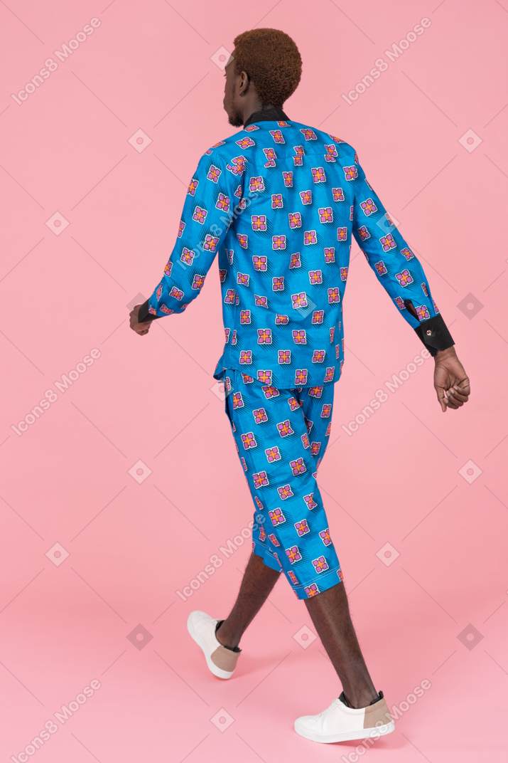 Hombre negro en pijama azul caminando sobre fondo rosa
