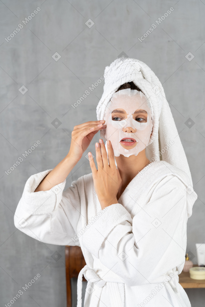 Woman in bathrobe applying a face mask