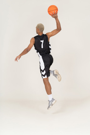 Three-quarter back view of a young male basketball player scoring a point