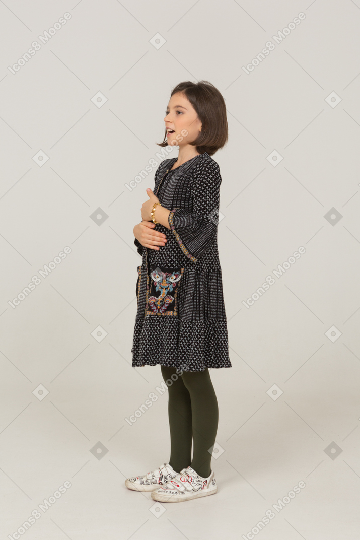 Vista de tres cuartos de una niña vestida mirando a un lado y tomados de la mano en el vientre