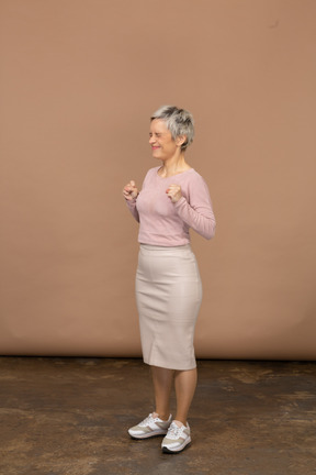 Vista lateral de uma mulher feliz em roupas casuais em pé com os punhos cerrados