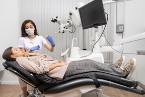 In voller länge einer zahnärztin, die einer patientin in einem krankenhausschrank einen zahnprototyp zeigt